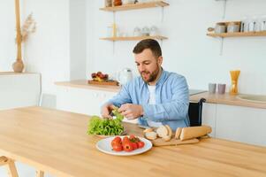 jovem Desativado homem sentado em roda cadeira preparando Comida dentro cozinha foto