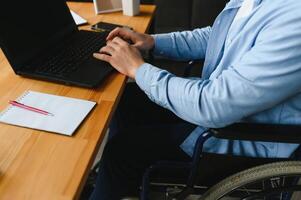 uma homem dentro uma cadeira de rodas é trabalhando dentro uma escritório. a conceito do trabalhos do pessoas com deficiências foto