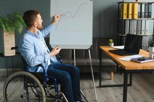 deficiente homem de negocios sentado em cadeira de rodas e usando computador dentro escritório foto