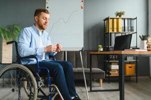 uma homem dentro uma cadeira de rodas é trabalhando dentro uma escritório. a conceito do trabalhos do pessoas com deficiências. foto