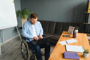 uma homem dentro uma cadeira de rodas é trabalhando dentro uma escritório. a conceito do trabalhos do pessoas com deficiências. foto