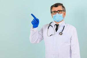 masculino doutor, dentro uma branco casaco e luvas, pontos para a lado com dele mãos. Próximo para a texto espaço. em branco em uma azul fundo. foto