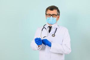 homem dentro médico luvas colocando em protetora face mascarar contra azul fundo. foto