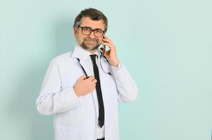 foto do médico médico vestindo branco casaco e estetoscópio segurando Móvel telefone em pé isolado sobre azul fundo.