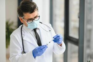 meio envelhecido masculino médico vestindo protetora mascarar segurando uma seringa com vacina. foto