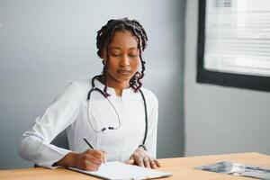 retrato confiante africano fêmea médico médico profissional escrevendo paciente notas isolado em hospital clínica corredor janelas fundo. positivo face expressão. foto