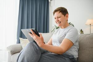 pessoas, tecnologia e Internet conceito - feliz meio envelhecido mulher com tábua pc computador às lar. foto