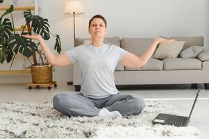 adulto mulher fazendo ginástica exercícios às lar. Senior mulher Faz alongamento exercícios. maduro mulher fazendo ioga poses foto