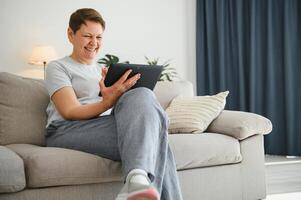 pessoas, tecnologia e Internet conceito - feliz meio envelhecido mulher com tábua pc computador às lar. foto