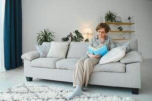 retrato do atraente focado alegre mulher sentado em divã lendo livro passatempo sonhar Acordado às casa casa plano interior. foto