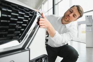 visitando carro concessionária. bonito barbudo homem é acariciando dele Novo carro e sorridente. foto