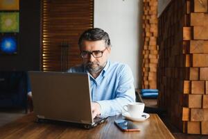 negócios, tecnologia e pessoas conceito , Senior homem de negocios com computador portátil computador bebendo café às moderno cafeteria. foto