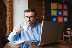 negócios, tecnologia e pessoas conceito , Senior homem de negocios com computador portátil computador bebendo café às moderno cafeteria. foto