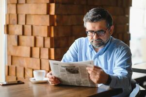 ativo Senior homem lendo jornal e bebendo café dentro restaurante foto