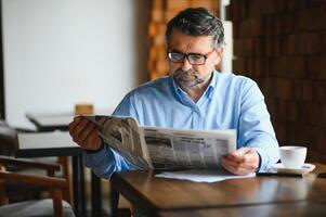 ativo Senior homem lendo jornal e bebendo café dentro restaurante foto