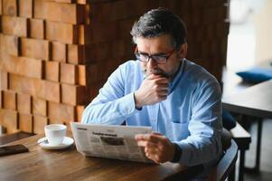 ativo Senior homem lendo jornal e bebendo café dentro restaurante foto