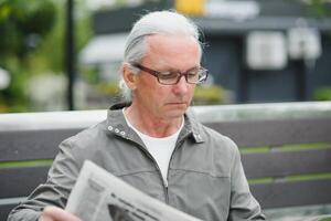 velho grisalho homem descansar em a Banco dentro verão parque foto