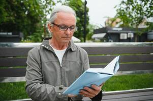 Senior homem lendo uma livro dentro a parque. foto