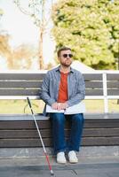 cego homem lendo braille livro, sentado em Banco dentro verão parque, em repouso foto