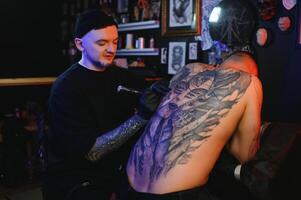 tatuagem artista demonstra a processo do obtendo Preto tatuagem com pintar. mestre trabalho dentro Preto estéril luvas foto