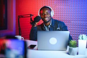 jovem africano americano homem gravação ou transmissão podcast usando microfone às dele pequeno transmissão estúdio. foto