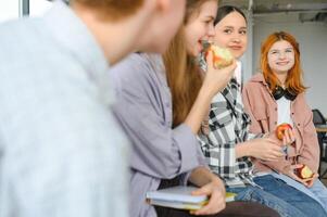 alegre alunos estão sentado às mesas e comendo a maçã durante uma pausa foto