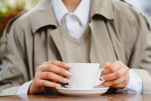 jovem à moda lindo mulher sentado dentro cidade cafeteria dentro rua, Primavera moda tendência estilo, bebendo café com leite, Rosa bolsa, saiu, emocional, feliz, sorridente foto