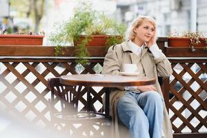jovem à moda mulher dentro vermelho boina tendo uma francês café da manhã com café e croissant sentado portas às a cafeteria terraço foto