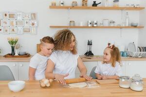 família Aprendendo Novo receita junto. feliz mãe e crianças mistura ingredientes para caseiro bolo, torta ou bolacha massa dentro a cozinha. foto