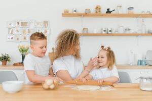 feliz família dentro a cozinha. mãe e crianças preparando a massa, assar biscoitos foto