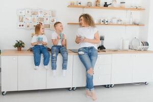 mãe com dela dois crianças sentado em a cozinha mesa. mãe com filha e criança pequena filho tendo café da manhã às lar. feliz estilo de vida família momentos. foto