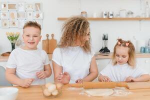 feliz família dentro a cozinha. mãe e crianças preparando a massa, assar biscoitos foto