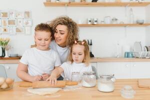 feliz família dentro a cozinha. mãe e crianças preparando a massa, assar biscoitos foto