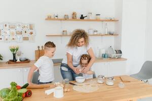 feliz família dentro a cozinha. mãe e crianças preparando a massa, assar biscoitos foto