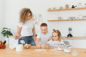 família Aprendendo Novo receita junto. feliz mãe e crianças mistura ingredientes para caseiro bolo, torta ou bolacha massa dentro a cozinha. foto