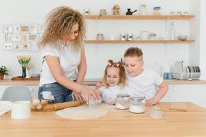 feliz família dentro a cozinha. mãe e crianças preparando a massa, assar biscoitos foto
