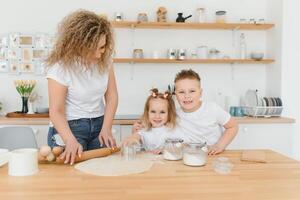 feliz família dentro a cozinha. mãe e crianças preparando a massa, assar biscoitos foto