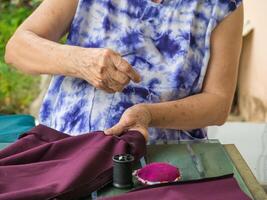 fechar-se do mãos Senior mulher tentando para fio uma agulha para de costura pano. espaço para texto. conceito do envelhecido pessoas e relaxamento foto