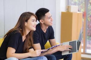 uma jovem casal sorridente e olhando às a computador portátil enquanto sentado em uma sofá dentro a escritório. o negócio sucesso a partir de trabalhos juntos Como uma equipe. conceito do o negócio e comércio eletrônico foto