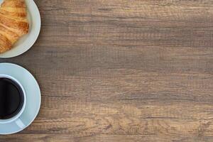 topo Visão do uma branco café copo e croissants em uma branco prato colocada em uma de madeira mesa. trabalhos a partir de lar. espaço para texto foto