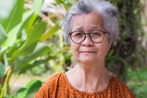 retrato do uma Senior mulher com curto cinzento cabelo vestindo copos, sorridente e olhando às a Câmera. espaço para texto. conceito do envelhecido pessoas e relaxamento foto