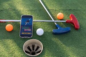 golfe equipamento em a verde grama. mini golfe Esportes apostando em uma Smartphone foto