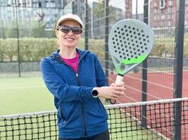 retrato do positivo jovem mulher com raquete e padel bola em tênis quadra foto