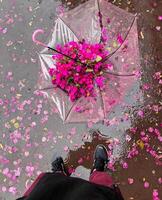 uma pessoa em pé em uma molhado calçada com a guarda-chuva preenchidas com Rosa flores foto
