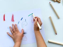 pequeno criança desenha com colori lápis em papel em branco mesa. foto