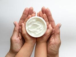 fechar acima do mulher e criança mãos segurando mão creme em branco fundo. cuidados com a pele e hidratante conceito. Projeto para assistência médica, beleza, bem-estar, e família Cuidado poster foto