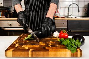 mãos do uma chefe de cozinha dentro Preto luvas corte a Berinjela em uma de madeira corte borda. fechar-se. foto