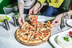 grupo do pessoas desfrutando pizza juntos às mesa foto