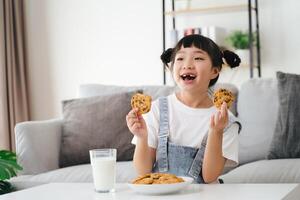 uma jovem menina é comendo biscoitos e bebendo leite foto