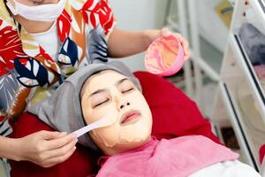 lindo jovem ásia mulher obtendo uma facial mascarar tratamento às a beleza salão. facial cuidados com a pele. foto